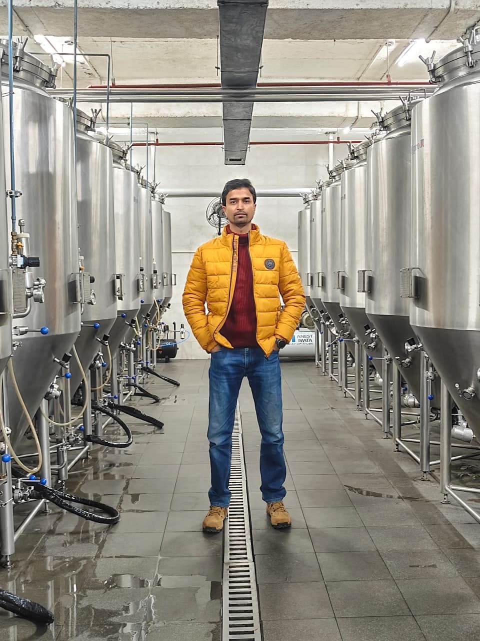 Gagan Deep standing between rows of stainless steel fermentation tanks in the brewery cellar